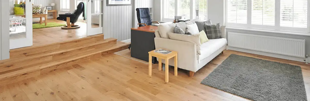 A modern living room with professionally installed laminate flooring, a beige sofa, a small side table, a gray rug, and large windows with white shutters in Columbia, SC